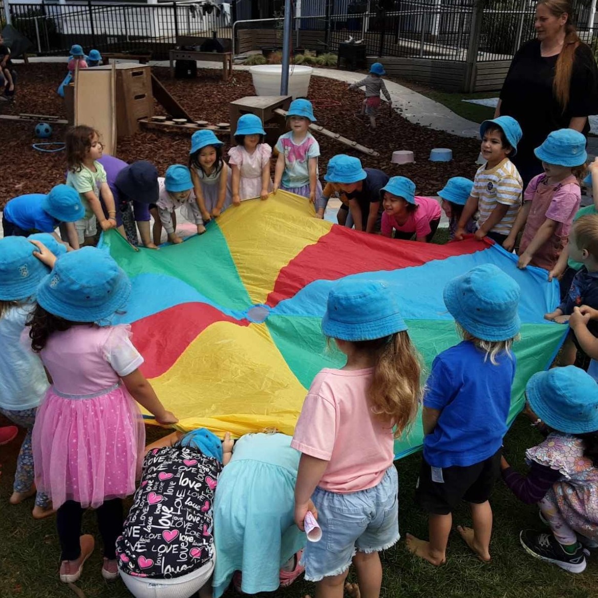 A cheerful outdoor playground filled with children playing on swings, climbing structures, and group games. The scene should depict laughter and joy, with greenery in the background, showcasing a nurturing and stimulating play environment.
